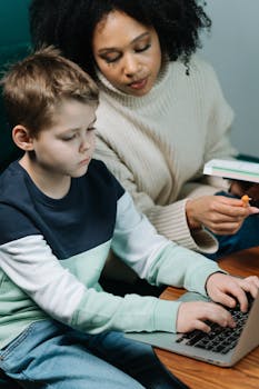 A dedicated tutor helps a young boy with his homework on a laptop, fostering learning.