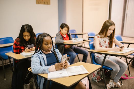A group of four students in a classroom using smartphones and notebooks during a lesson.