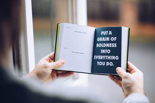 A person holds an open journal with a motivational quote by a window.