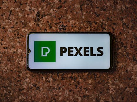 A smartphone displaying the Pexels app logo on a granite tabletop.