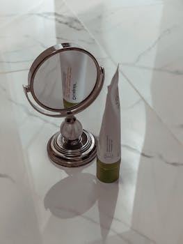 Close-up of a cosmetic tube and mirror on a marble surface, showcasing sleek design.