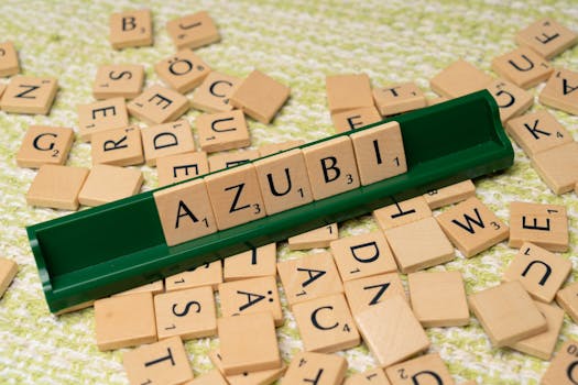 Close-up of wooden letter tiles forming the word 'Azubi' on a green rack with scattered tiles.