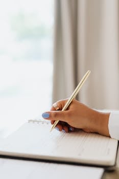 Hand holding a pen poised over a lined notebook page, suggesting planning or journaling.