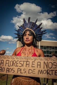 Indigenous woman protesting with traditional headdress and sign against deforestation.